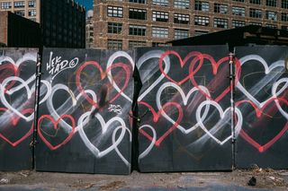 A boarded up fence graffitied with red and white hearts