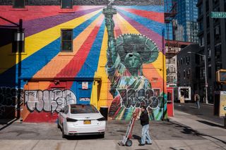 Worker with hand truck walking past mural on building showing Statue of Liberty wearing a sombrero