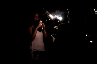 A person holds a sparkler while another takes a photo of them on a smartphone