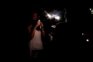 A person holds a sparkler while another takes a photo of them on a smartphone