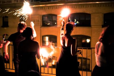 Several people waving sparklers with neighboring apartment building in the background