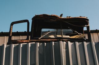 The front windshield of a derilict truck appearing over the top of a metal fence