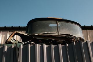 The front windshield of a derilict truck appearing over the top of a metal fence